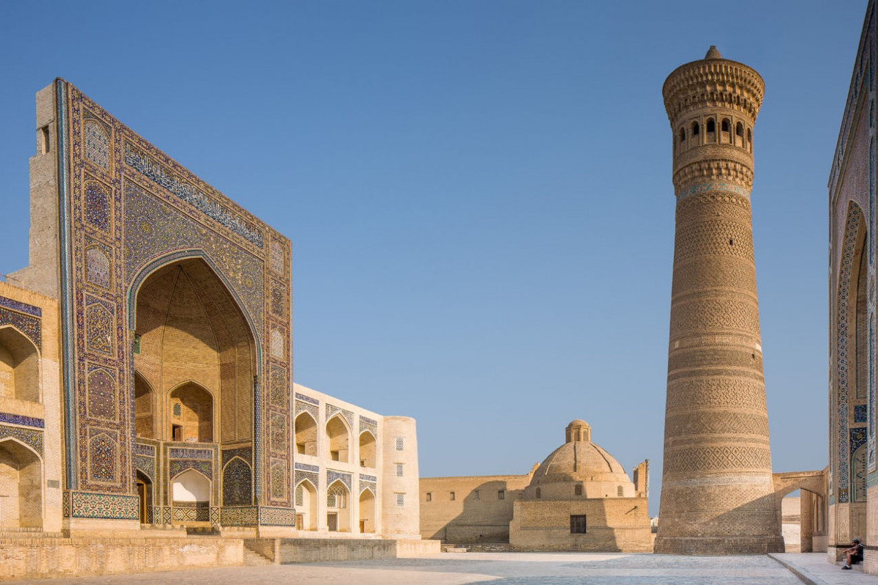 Exterior de Mir-i-árabe Medressa e Kalon Minaret. Dois turistas estão sentados na entrada para Kalon Mosque. Foto tomada em Bukhara, no Uzbequistão.